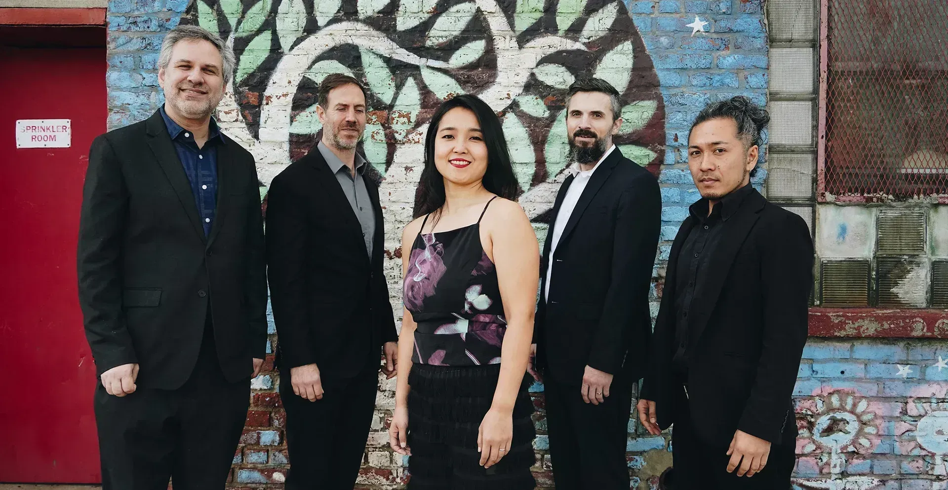 Five people in formal attire standing in front of a colorful mural wall