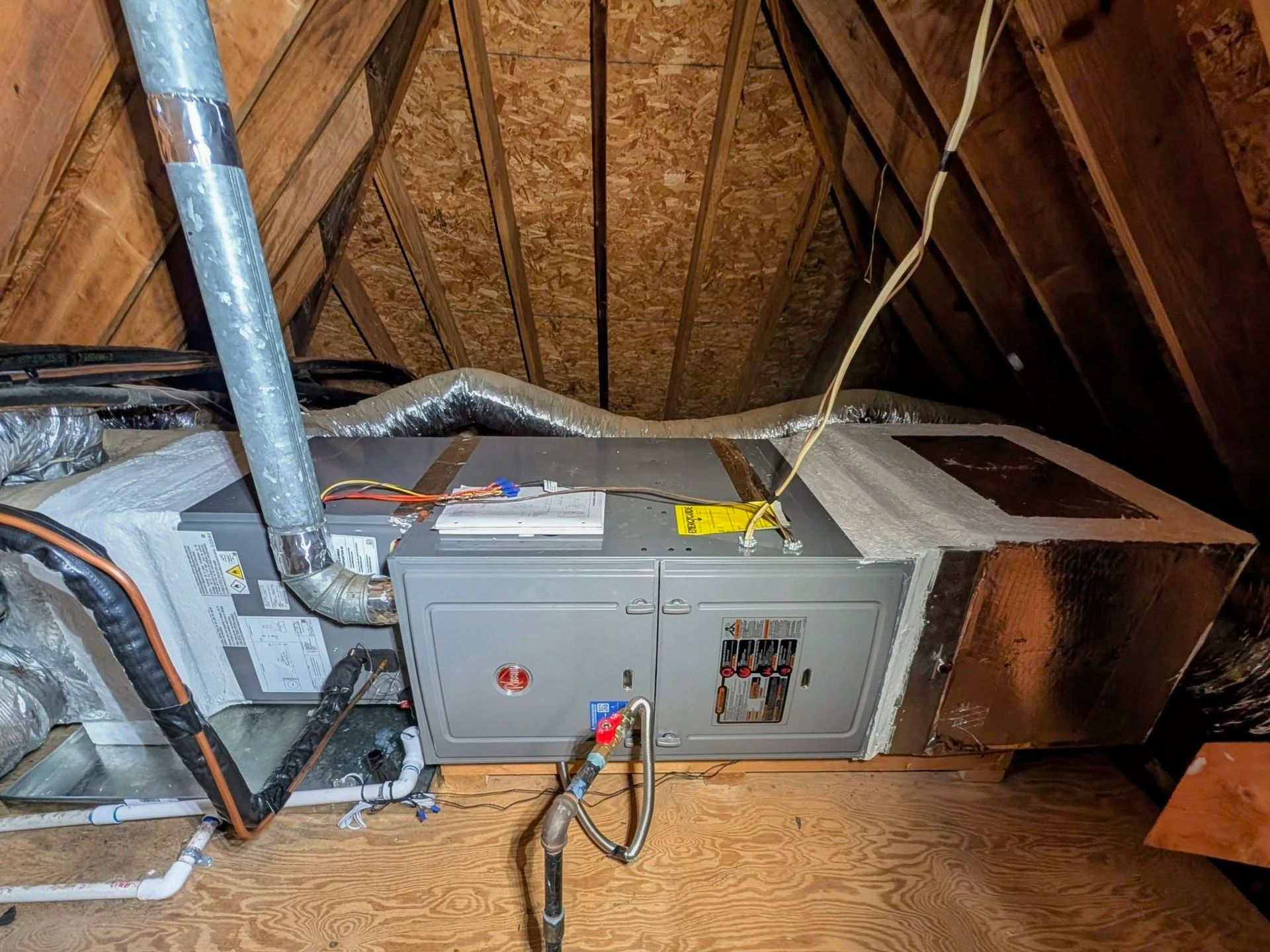 HVAC unit and ductwork in an attic with exposed wooden rafters and insulation