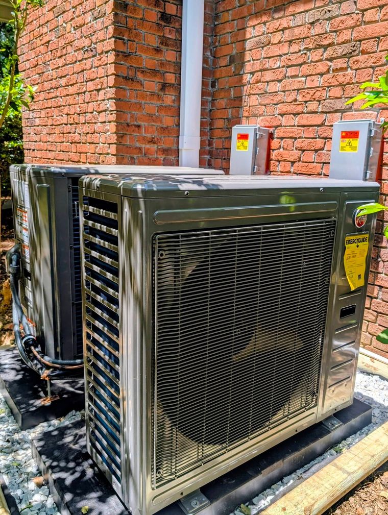 Outdoor HVAC unit beside a brick building with two electrical boxes mounted above it