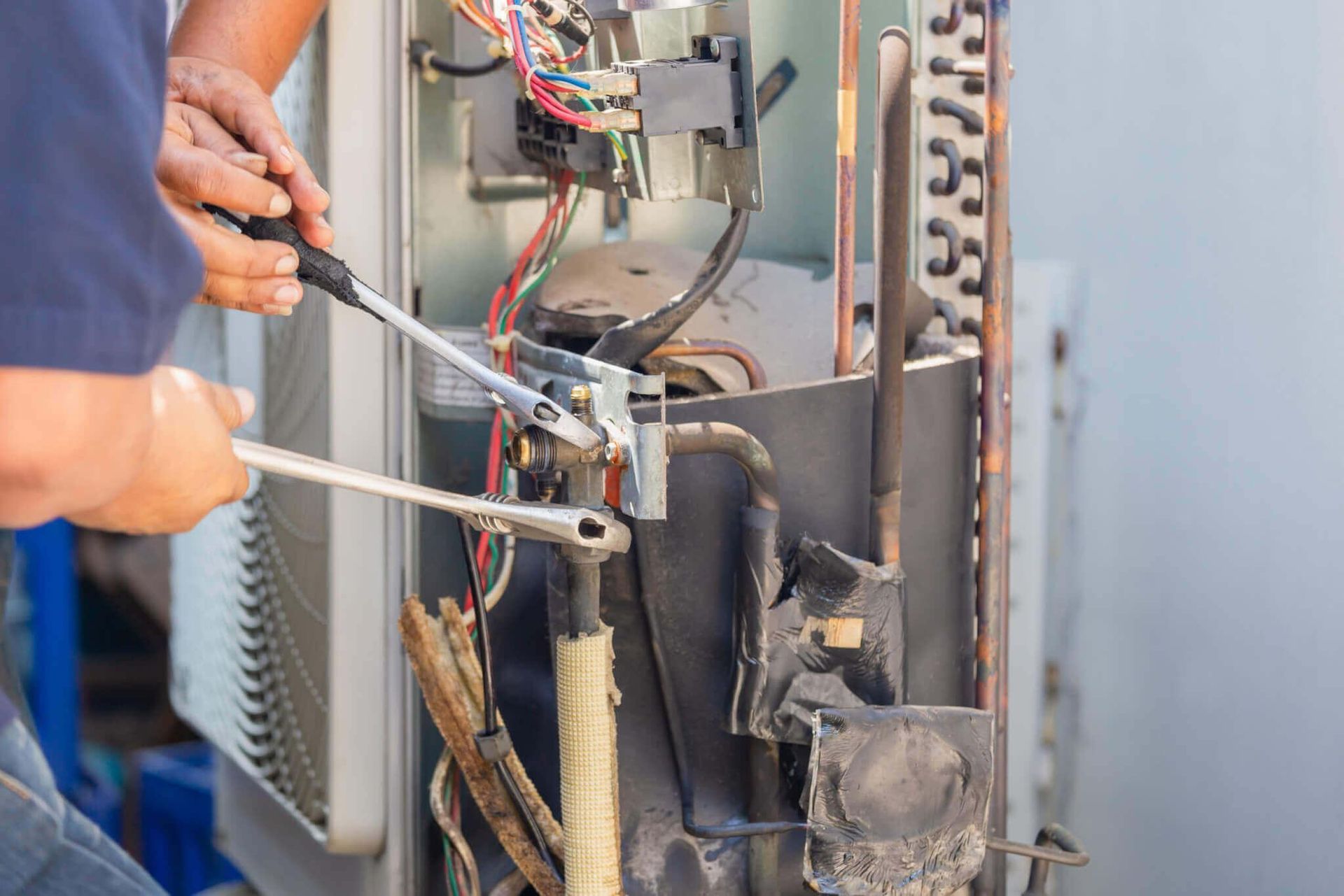 Technician repairing HVAC unit with tools and exposed wiring inside a metal panel.