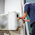 Technician servicing an outdoor air conditioner unit with tools on a wall mount