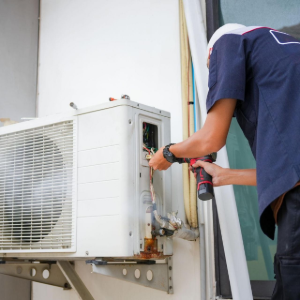Technician servicing an outdoor air conditioner unit with tools on a wall mount