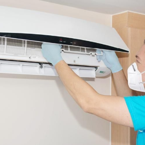 Technician in gloves cleaning the indoor unit of a wall-mounted air conditioner