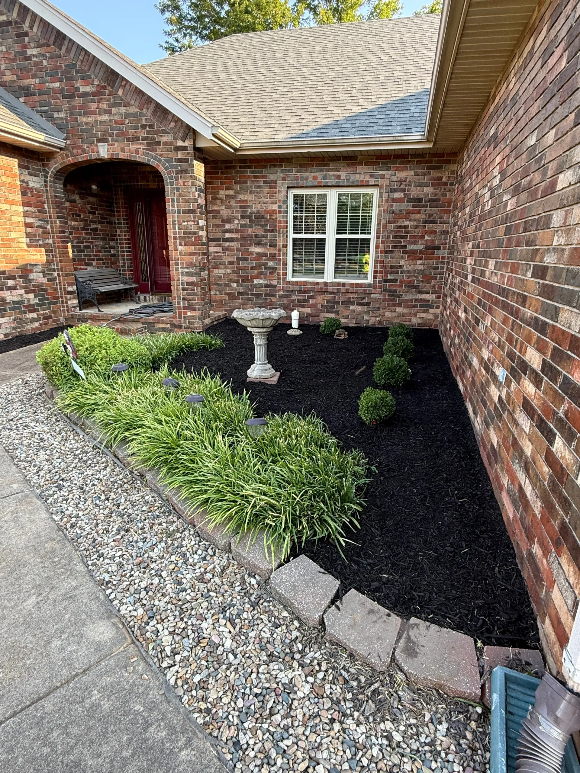 A red brick house exterior featuring a front garden with black mulch, green shrubs, and a birdbath in springfield