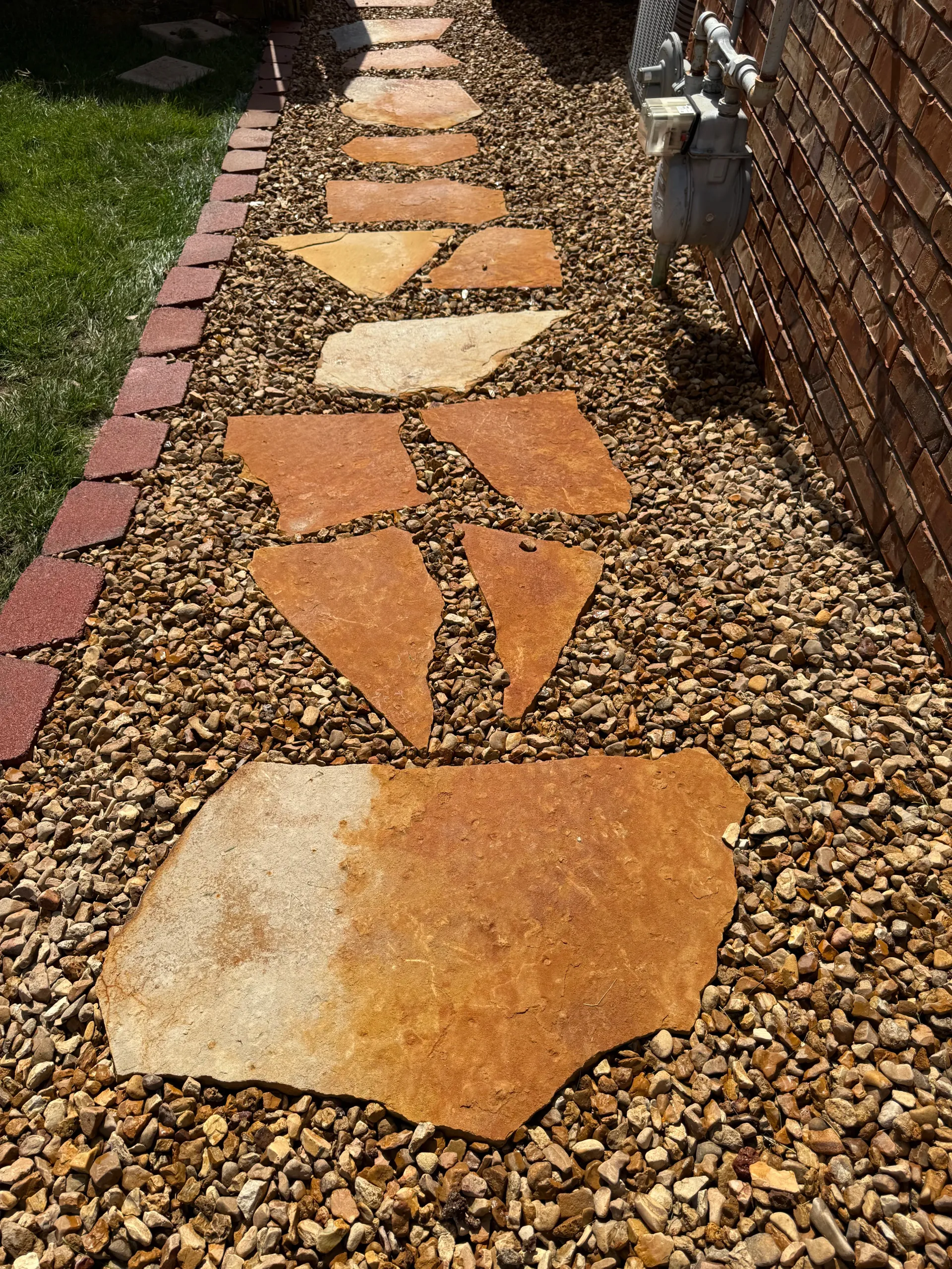 A stone stepping-stone path set in gravel alongside a brick wall and a patch of grass in ozark mo