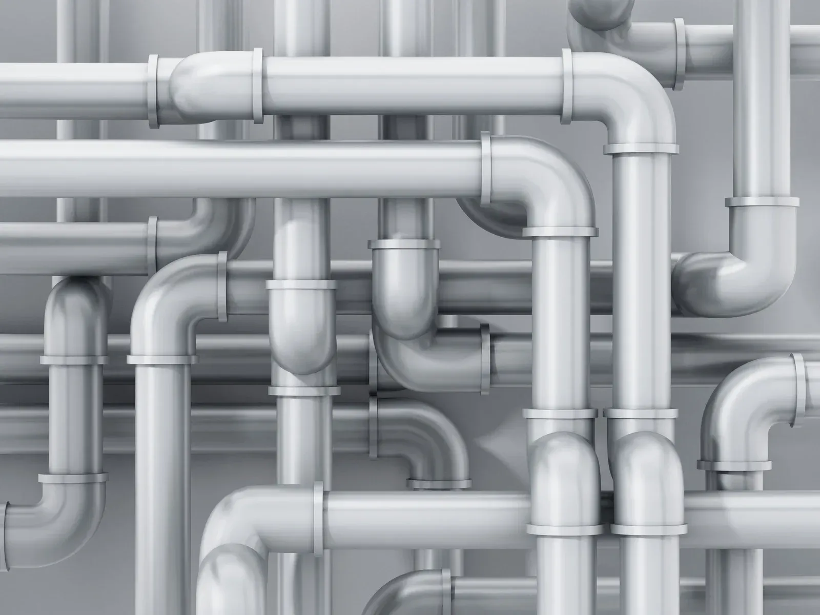 Gray industrial pipes with elbows and joints running across a plain wall.