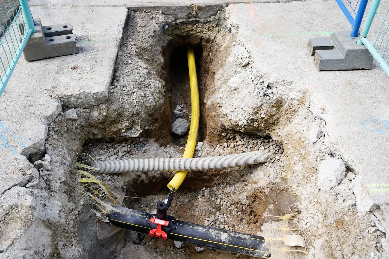 Yellow cable in a trench with exposed pipes and a red clamp on gravel ground