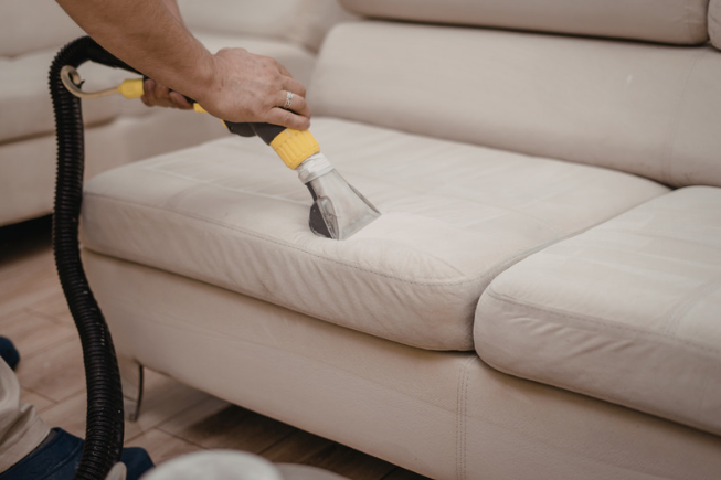 Person cleaning a beige sofa with a vacuum upholstery attachment