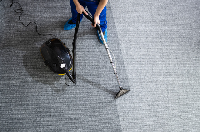 Person using a carpet cleaner on gray carpet with a black vacuum unit nearby