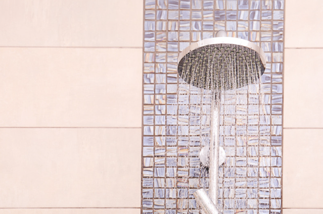 Showerhead running water against blue mosaic tile in a tiled bathroom shower