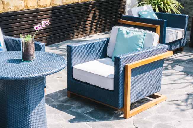 Outdoor patio with blue-gray wicker sofa, matching chair, and round table in sunlight