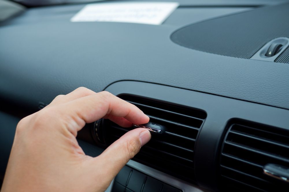 Hand adjusting the air conditioning vent on a car dashboard inside a car's interior