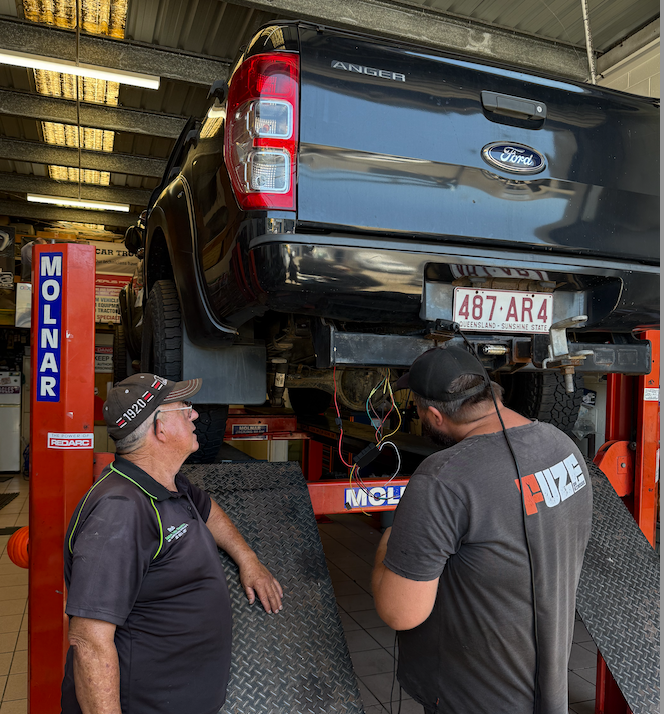 A Ute Up On A Winch With Two Mechanics Looking Into The Breaks— Cabba Auto Electrics In Chinderah, NSW