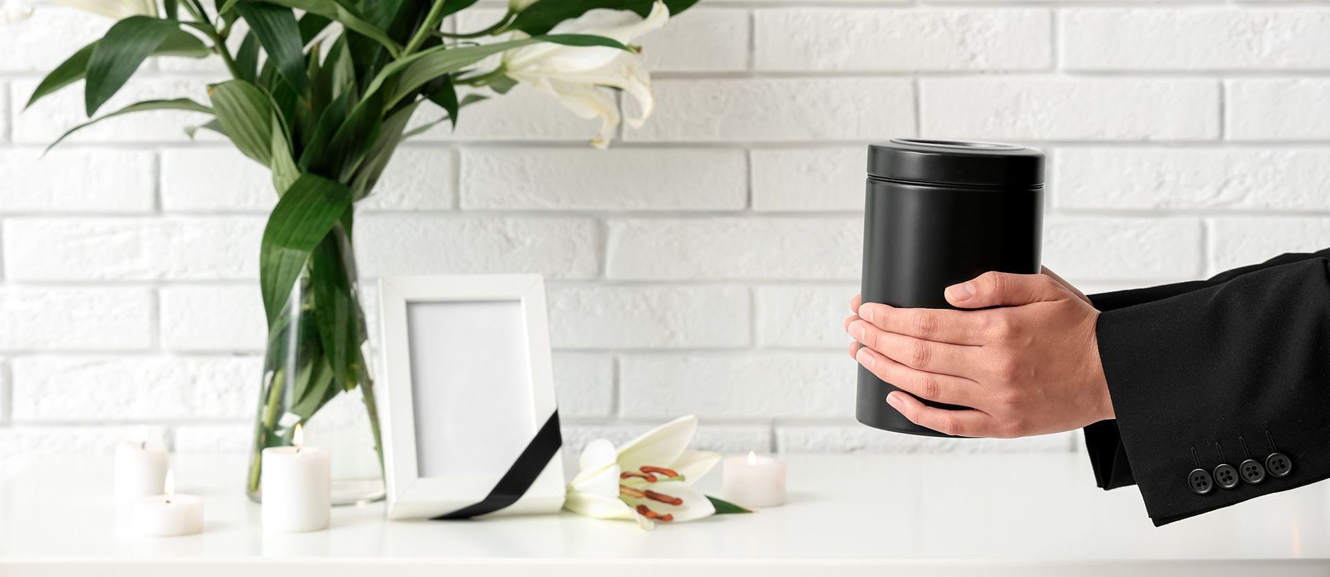A man in a suit is holding a black urn in front of a vase of flowers.