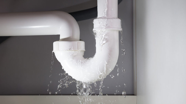 A white U-shaped plumbing pipe under a sink leaking water from its joints.