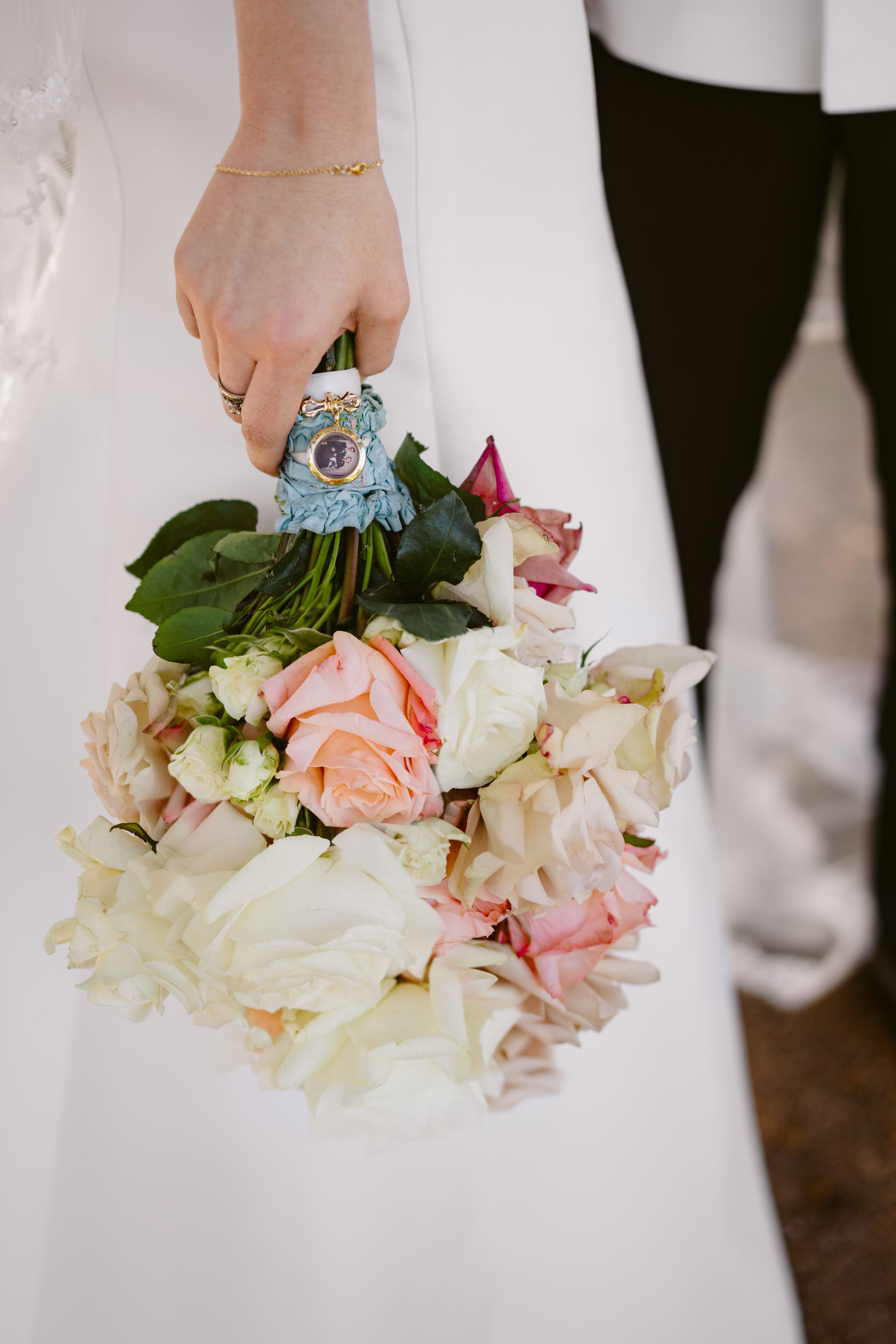 Hand holding a white and peach floral bouquet against a white dress