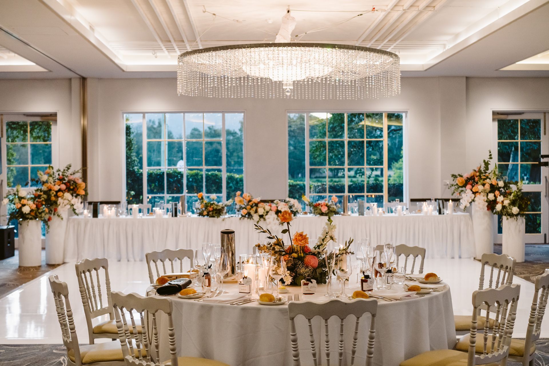 Elegant banquet hall set for a formal dinner with white tablecloths, chandeliers, and floral centerpieces