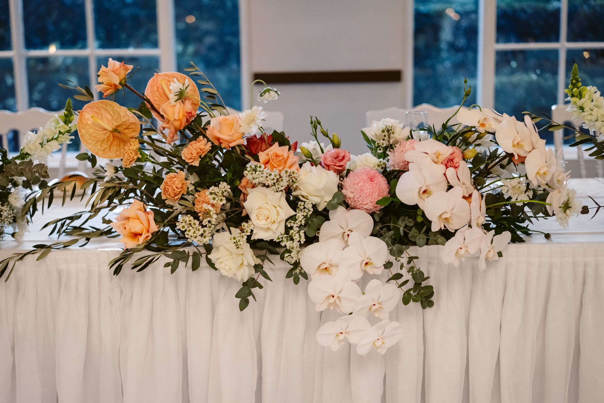Floral wedding reception centerpiece with white, peach, and pink flowers on a draped table