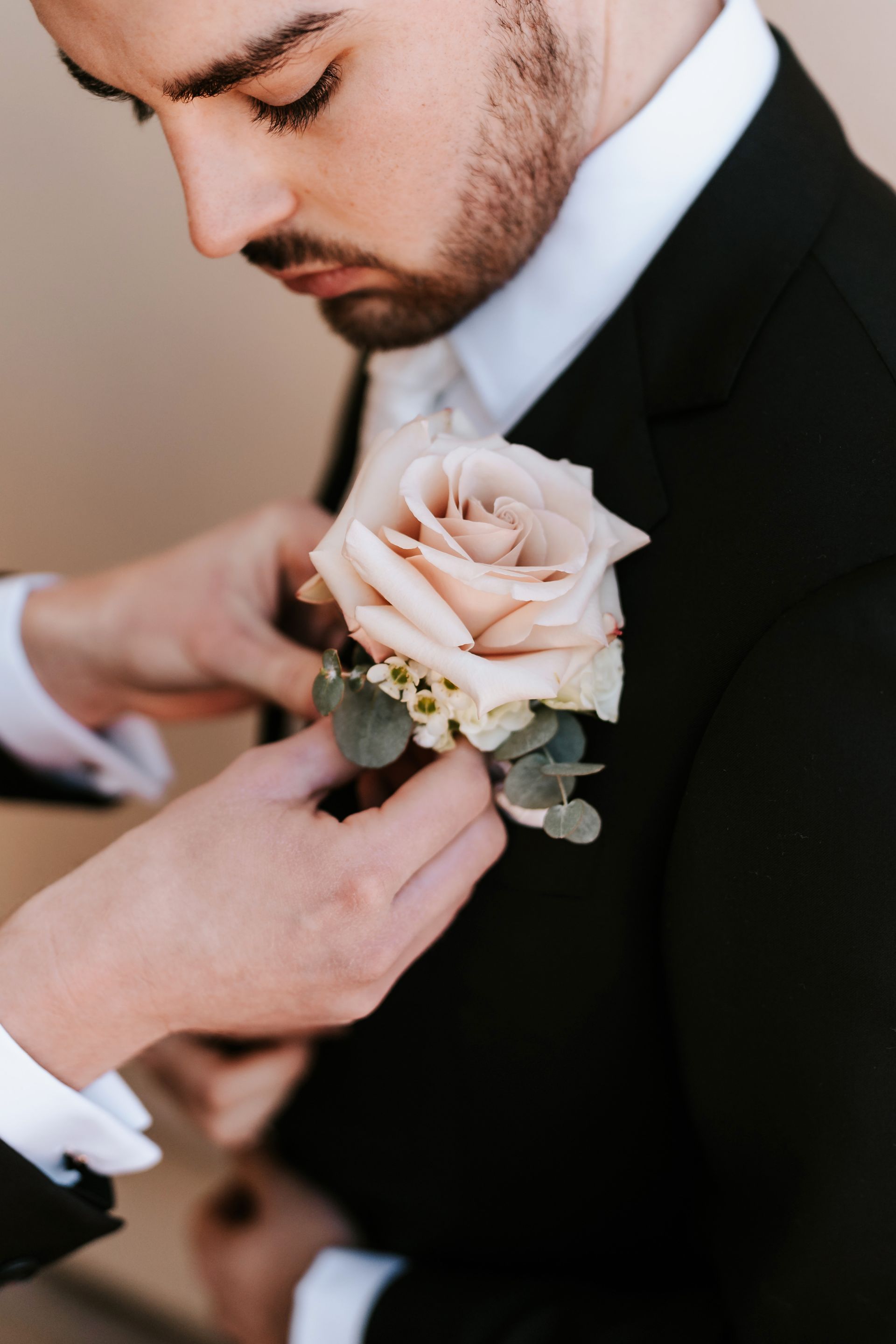 Hands adjusting a pale pink boutonniere on a black suit jacket