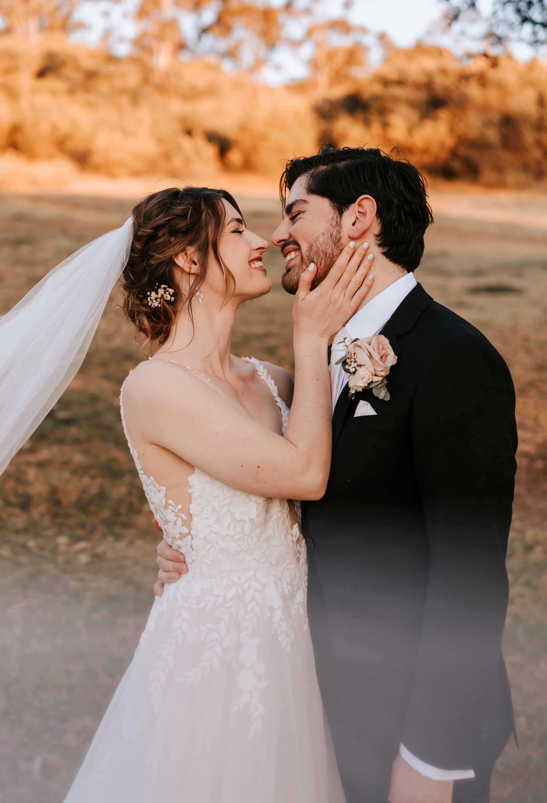 Bride and groom embracing outdoors at sunset, smiling and touching faces