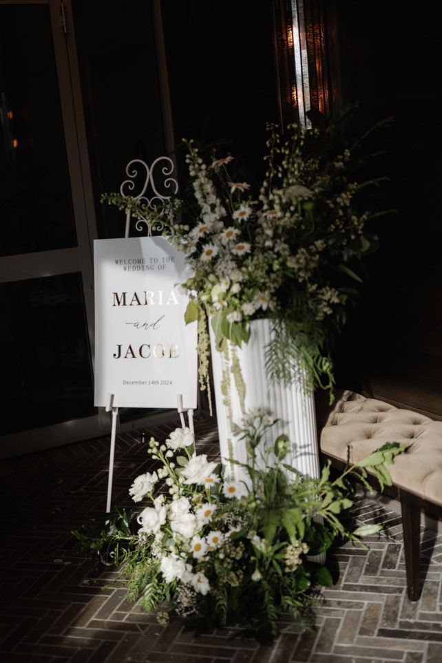Floral wedding welcome sign with white flowers and greenery in a dark venue entrance