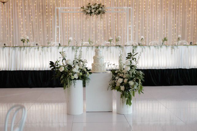 Elegant white wedding stage with floral arrangements, candles, and a blush-and-gold backdrop