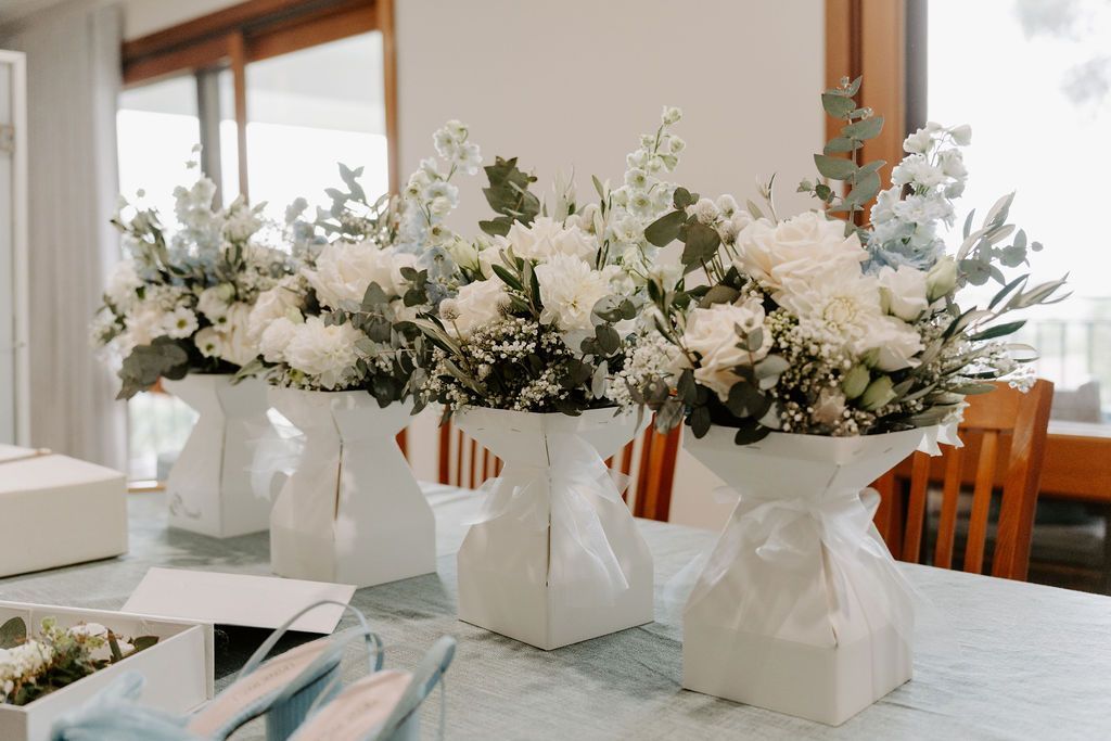 White floral centerpieces in paper bags arranged on a dining table in a bright room