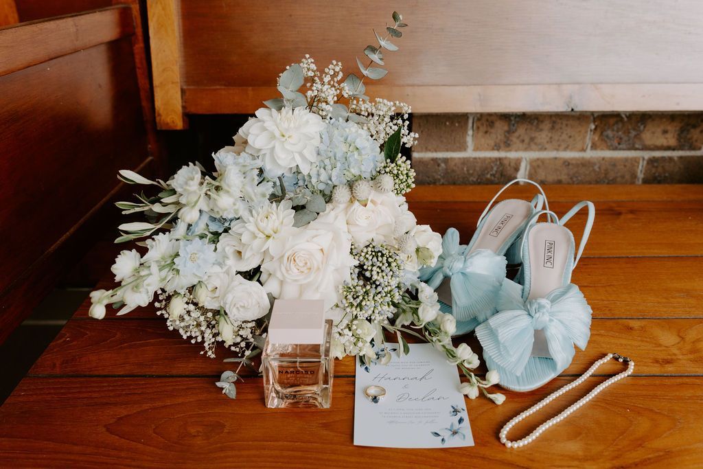 White floral arrangement with bridal accessories and invitation on a wooden floor