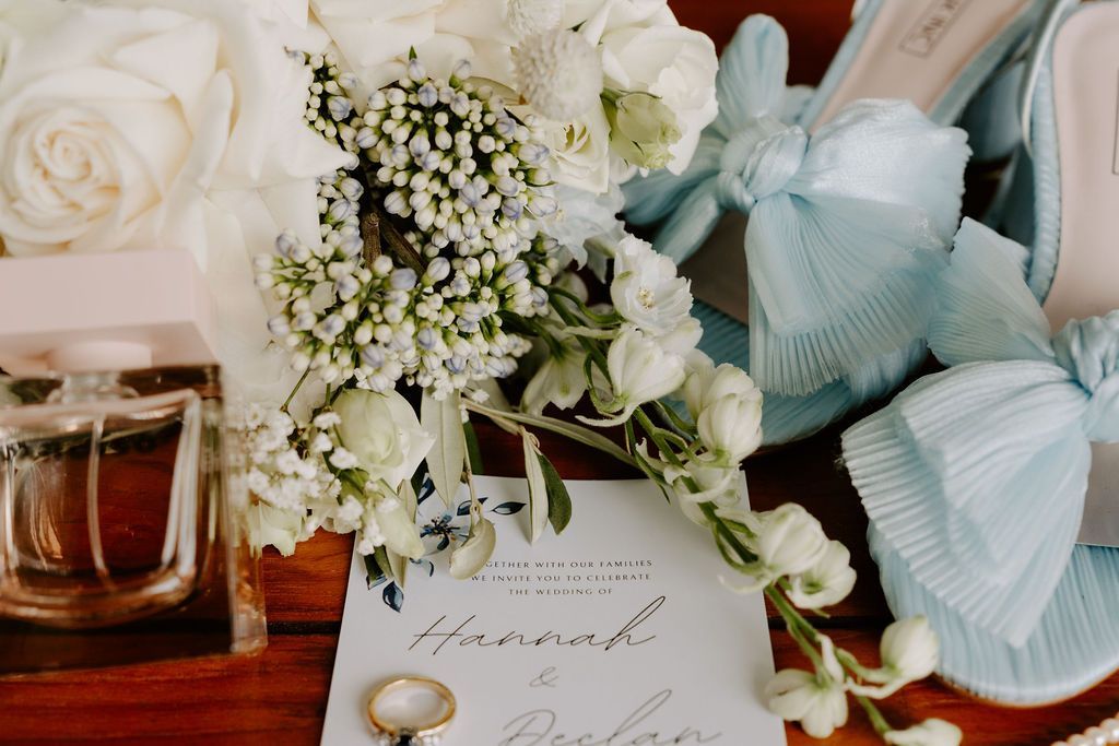 Floral bridal flat lay with white roses, perfume bottle, and pale blue ribbon on a wooden table