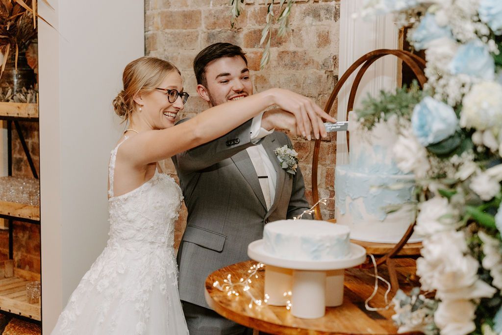 Bride and groom cutting a white cake at a rustic wedding reception with floral décor