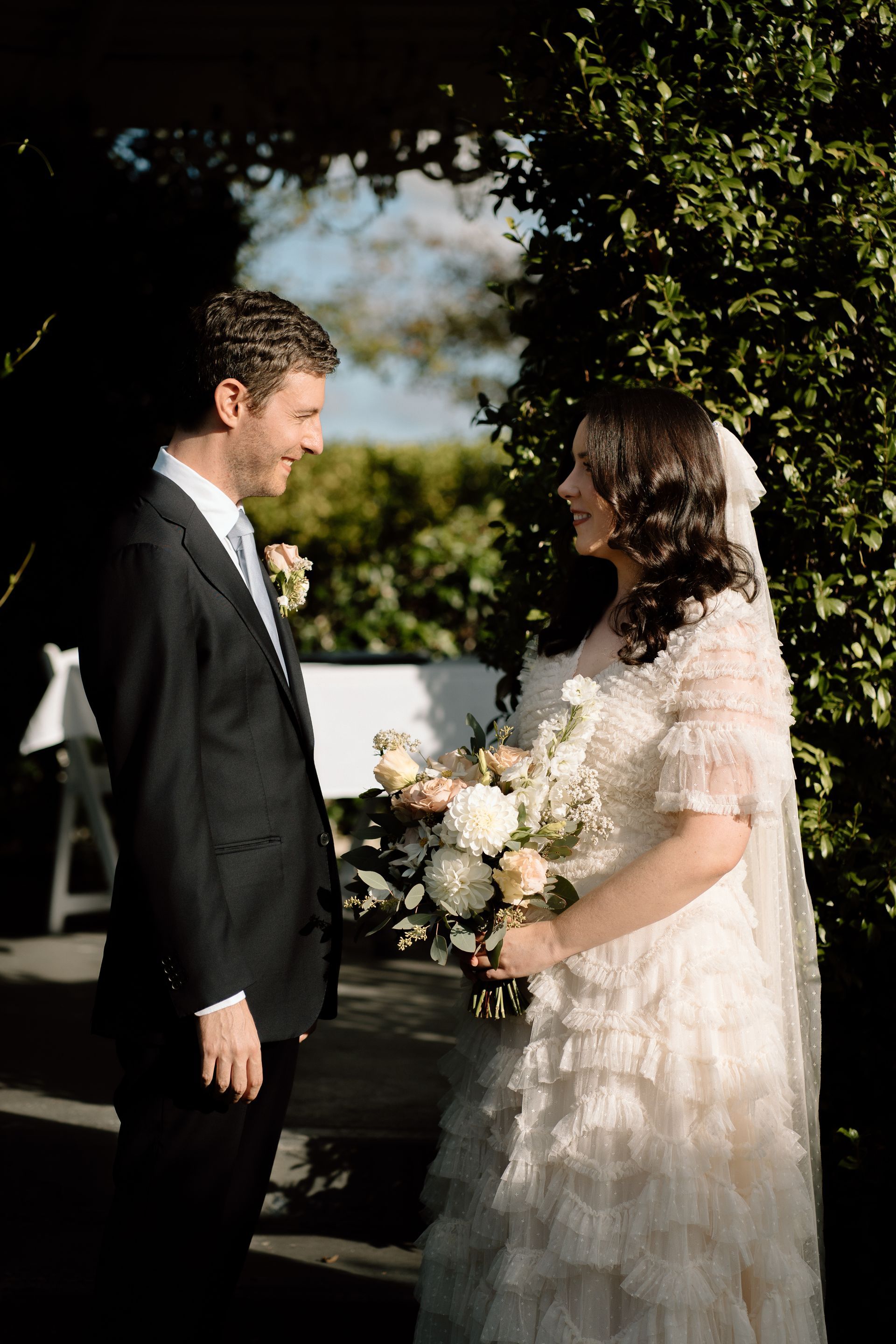 Bride and groom standing outdoors, facing each other during a wedding ceremony.