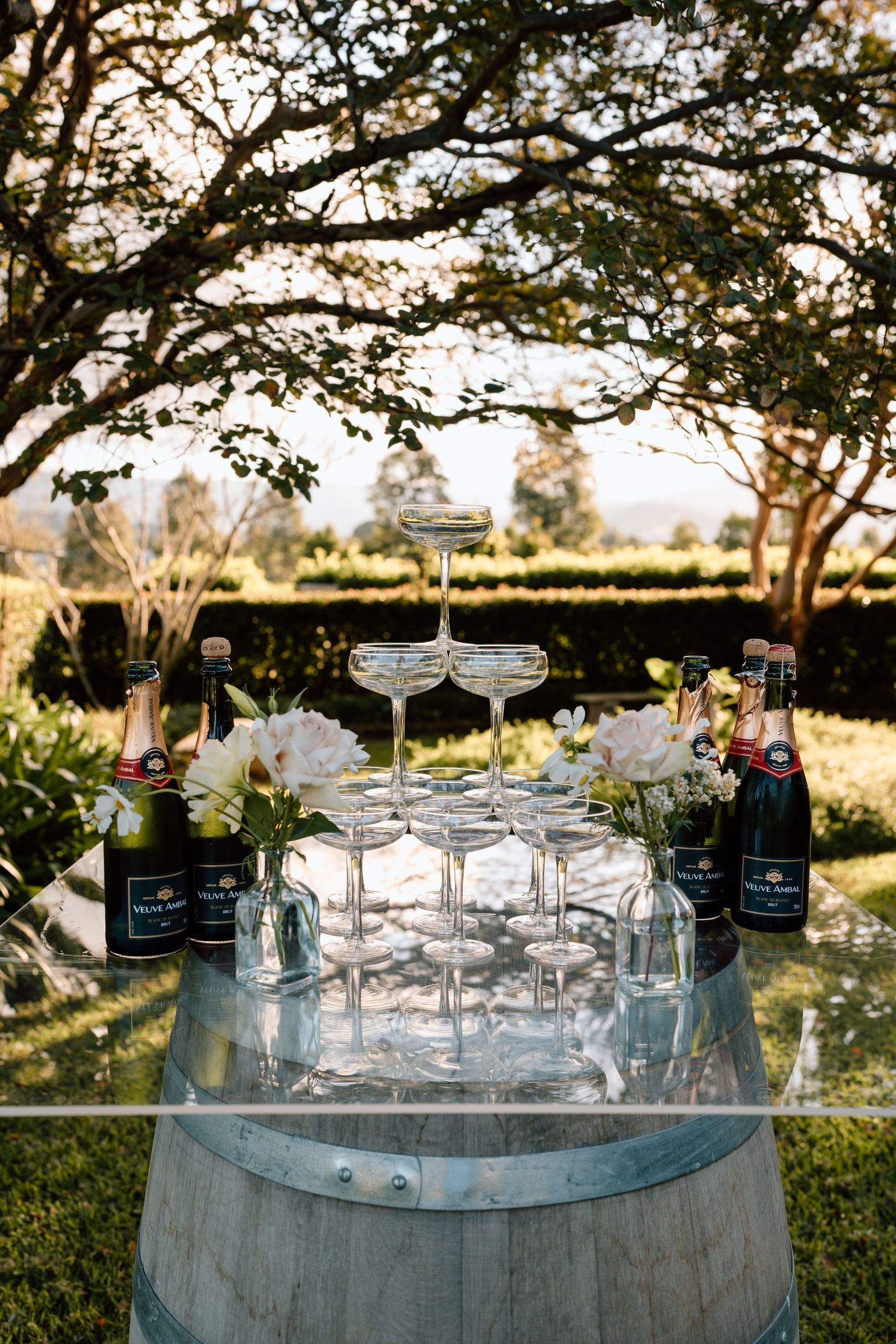 Outdoor champagne tower on a barrel table with wine bottles in a garden setting