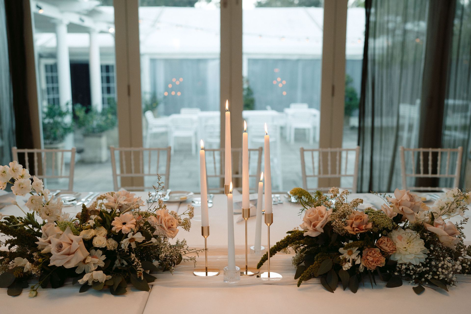 Floral wedding table centerpiece with white candles in a bright glass-walled venue