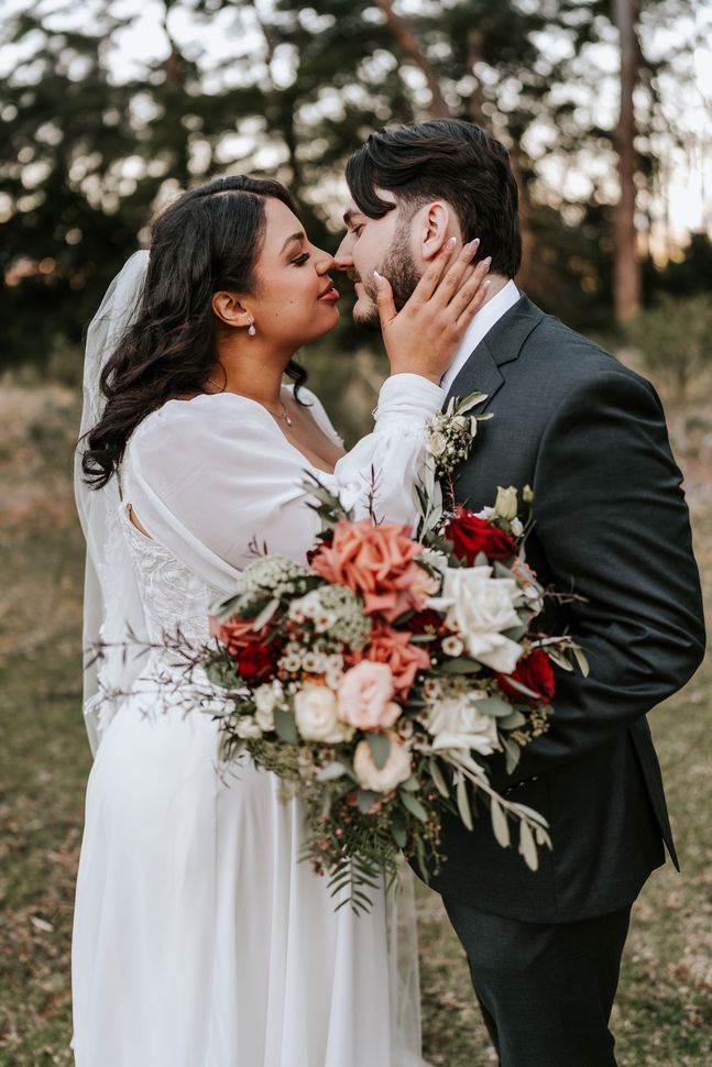 Couple kissing outdoors, holding a bouquet of white and coral flowers.