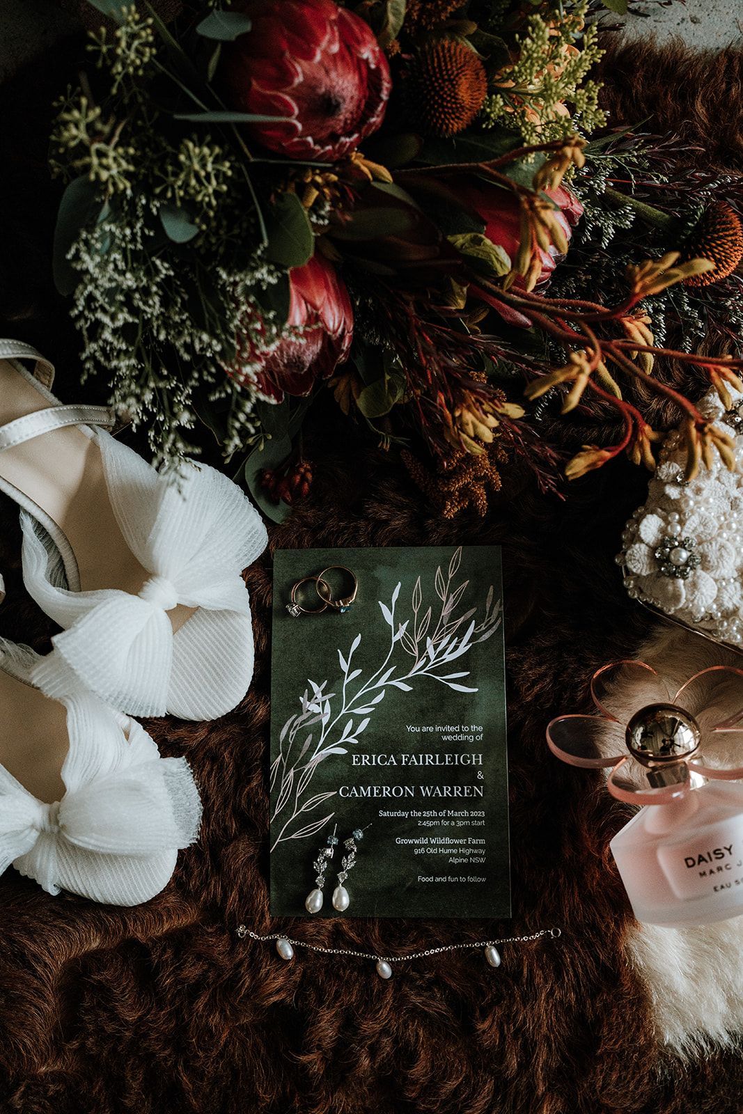 Dark floral invitation suite with white ribbon, red blooms, and candles on a fur-textured surface
