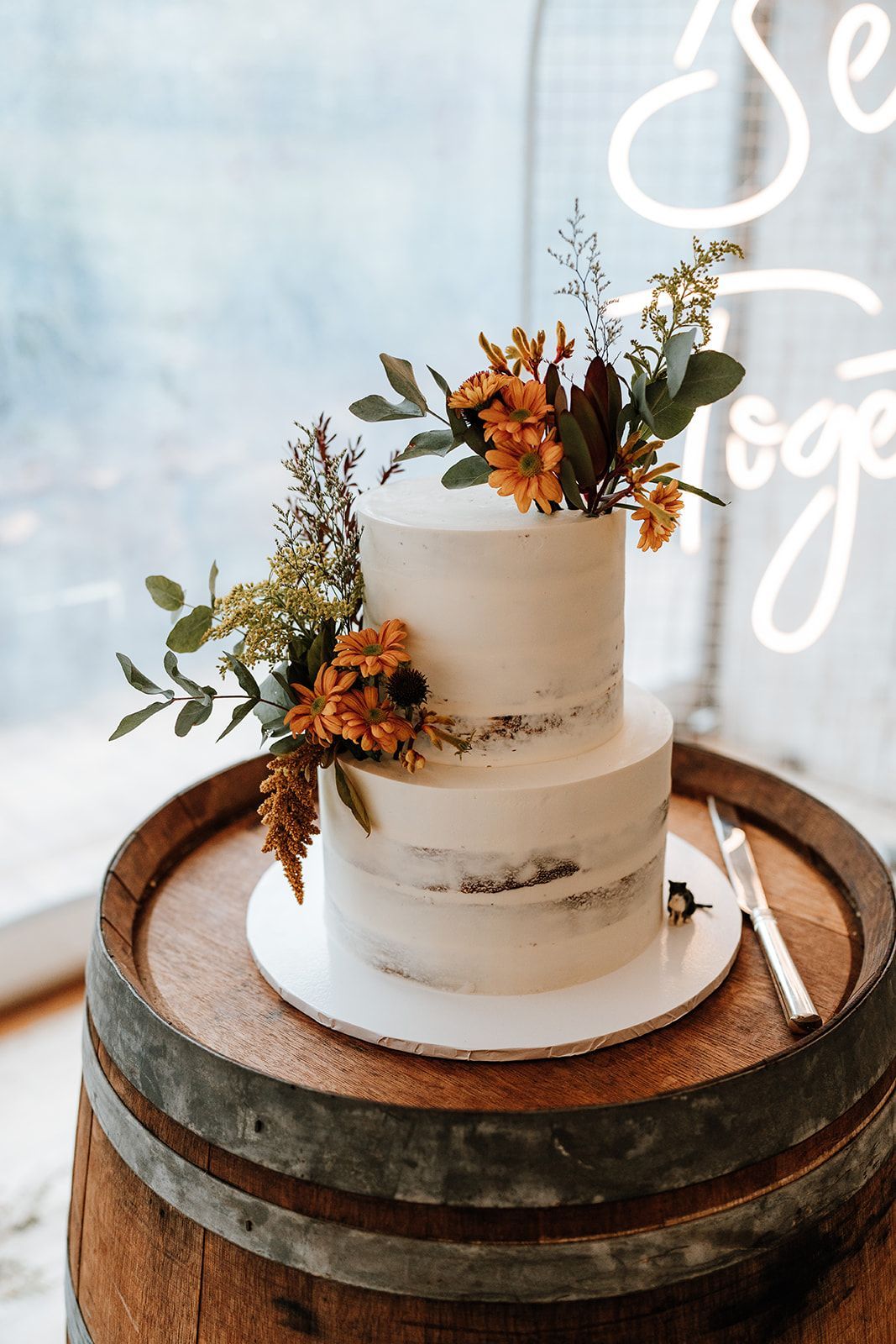 Two-tier white wedding cake with orange flowers on a wooden barrel table