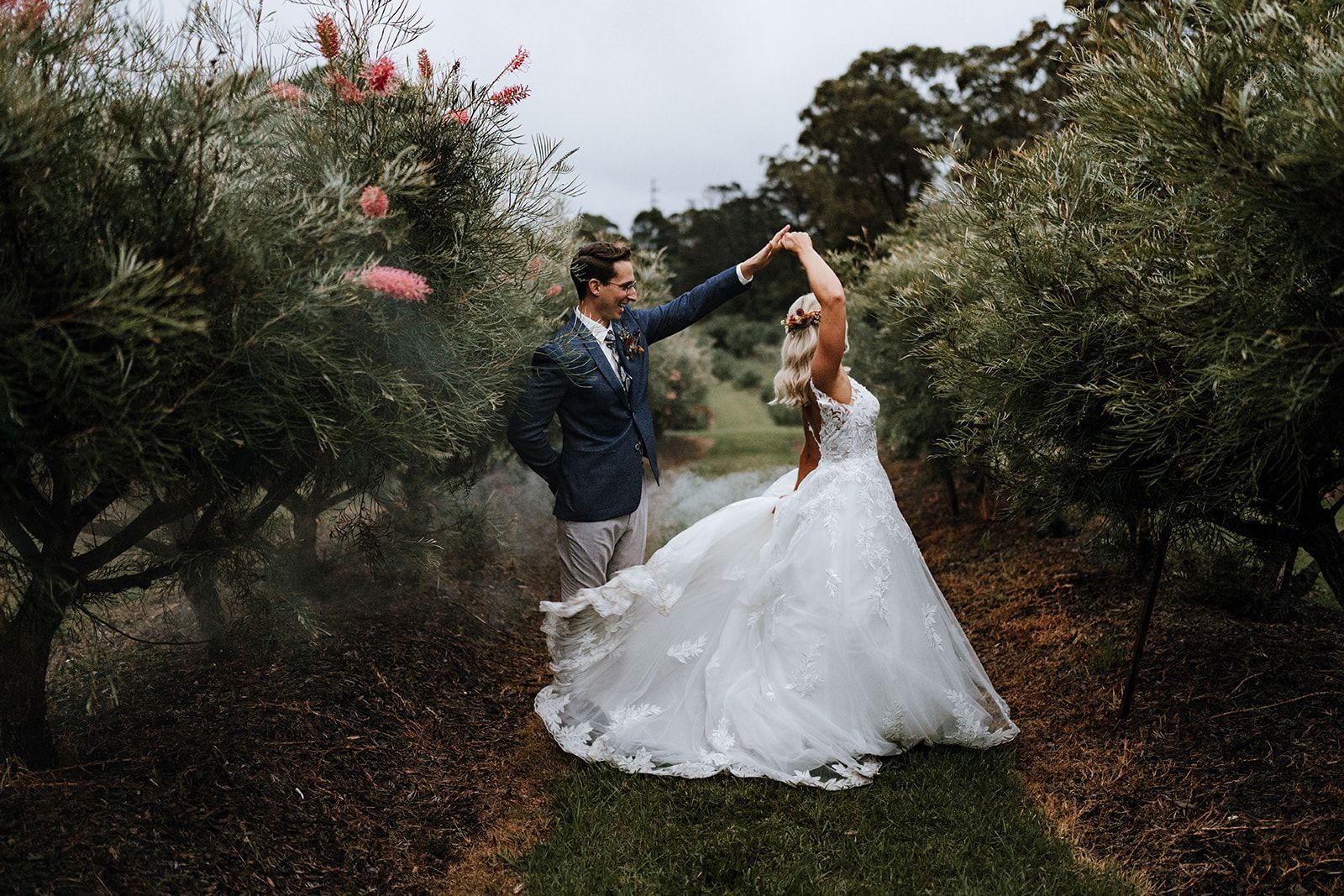 Bride and groom dancing outdoors in a garden, with the bride in a white gown and the groom in a blue suit