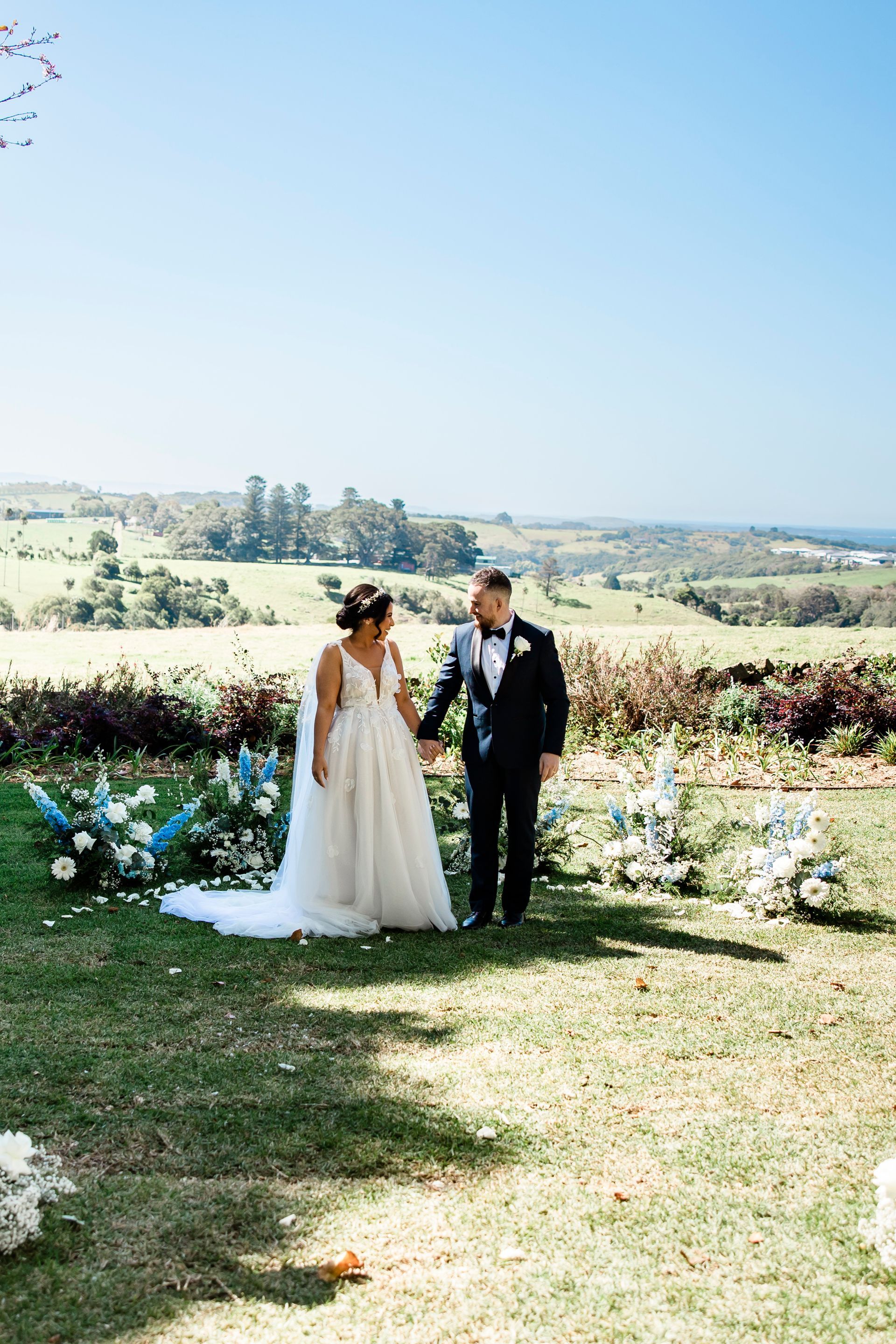 Bride and groom standing outdoors in a sunny garden with a scenic countryside view