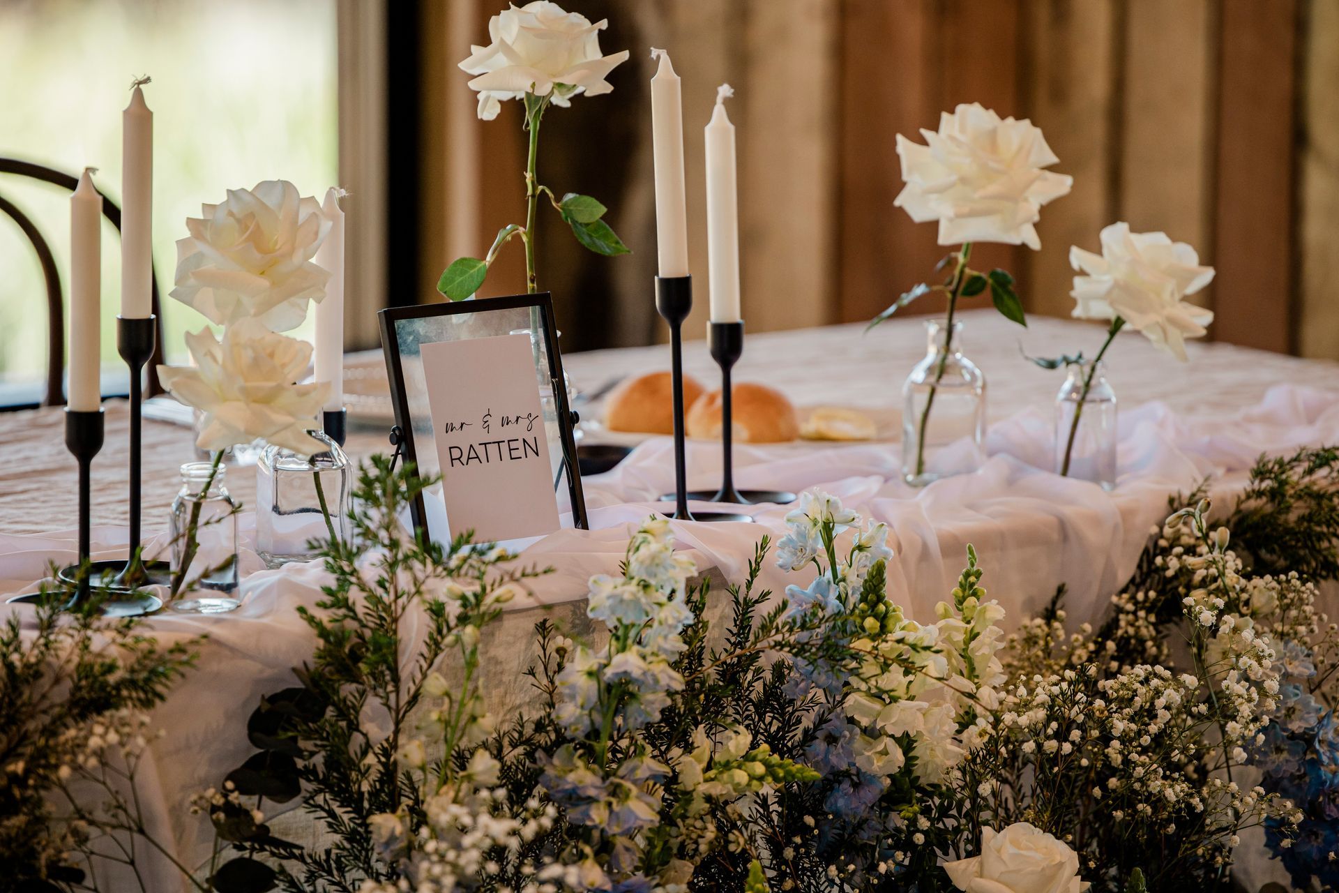 White floral wedding memorial table with candles, framed sign, and greenery on a draped cloth.