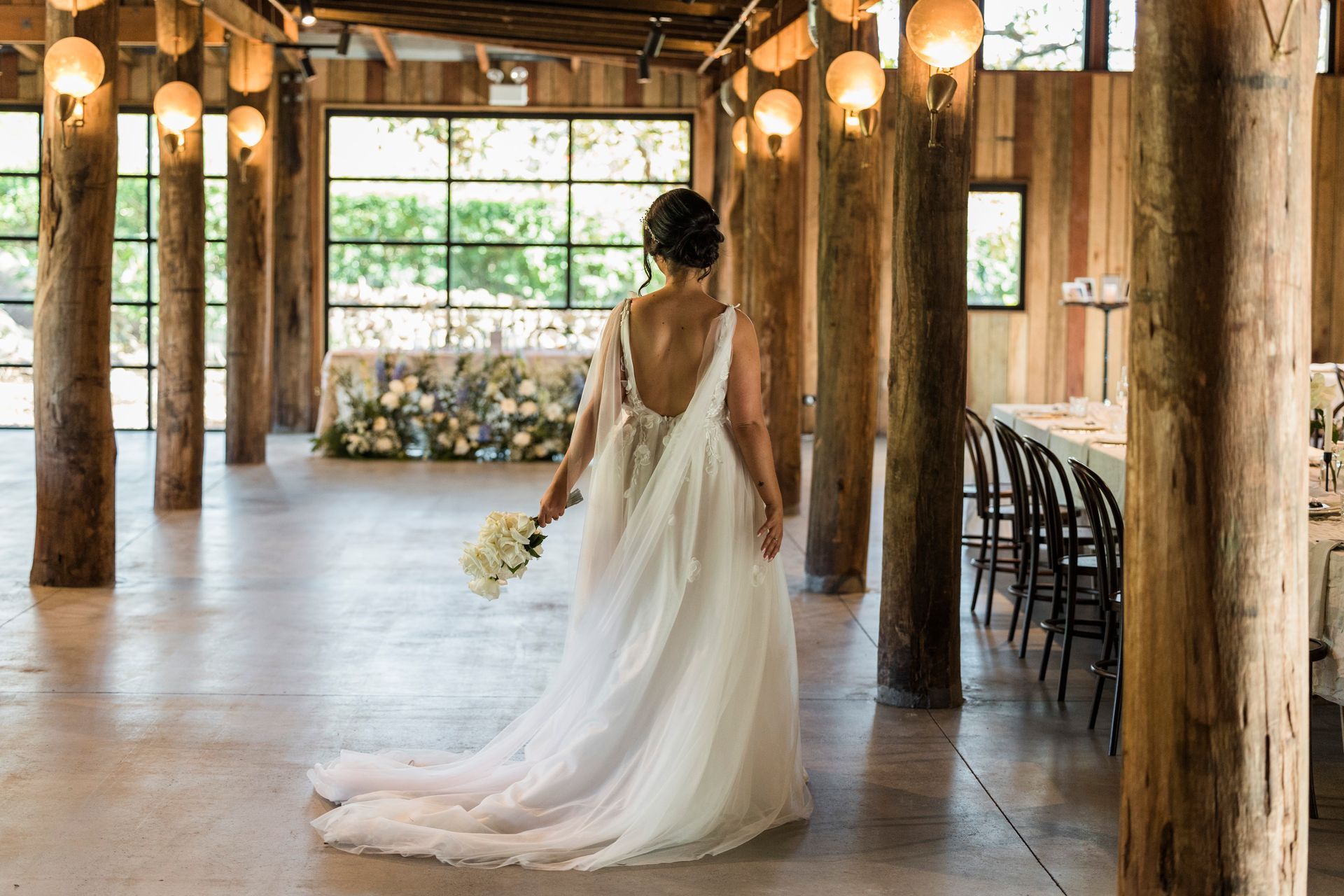 Bride in flowing white gown walking through a rustic barn venue with warm hanging lights
