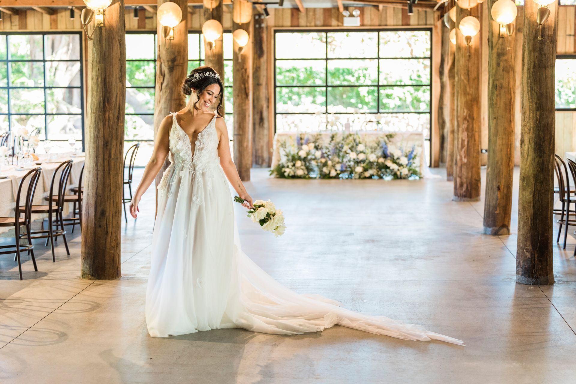 Bride in white gown holding bouquet in a rustic barn wedding venue