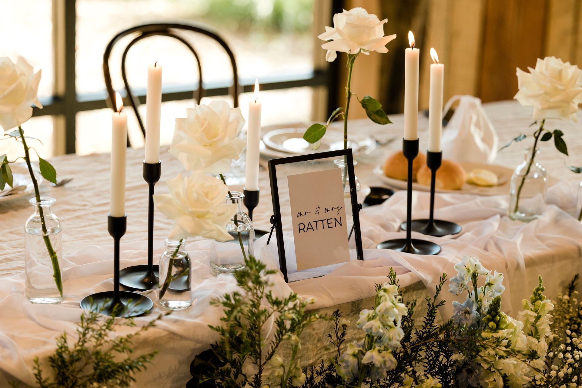Elegant wedding table centerpiece with white flowers, candles, and a framed table number on a softly lit table