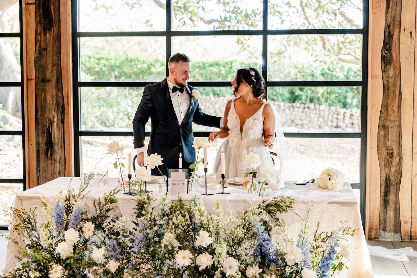 Bride and groom toasting at a decorated wedding reception table by large windows