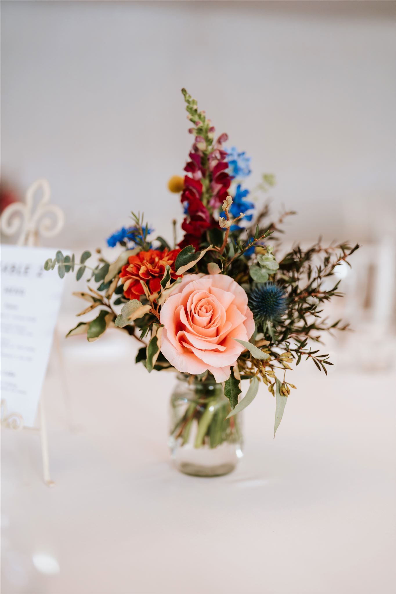 Pink and blue floral arrangement in a glass vase on a white table