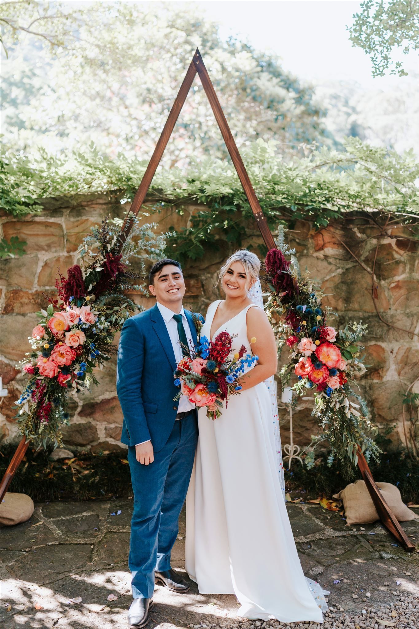 Bride and groom stand beneath a floral arch in an outdoor garden wedding setting