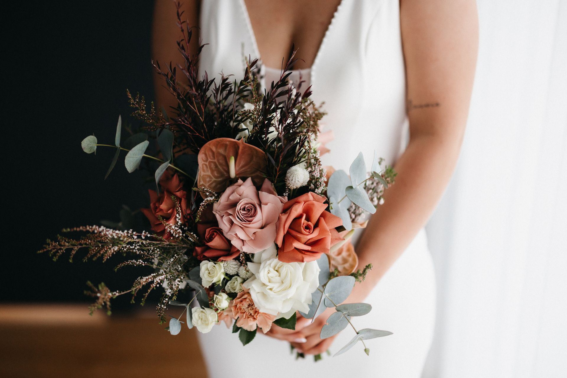 Bridal bouquet of pink, peach, and white flowers held against a white dress