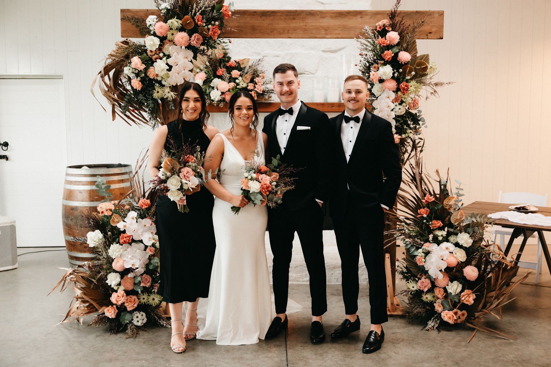 Four people posing at a wedding arch with white and peach floral arrangements