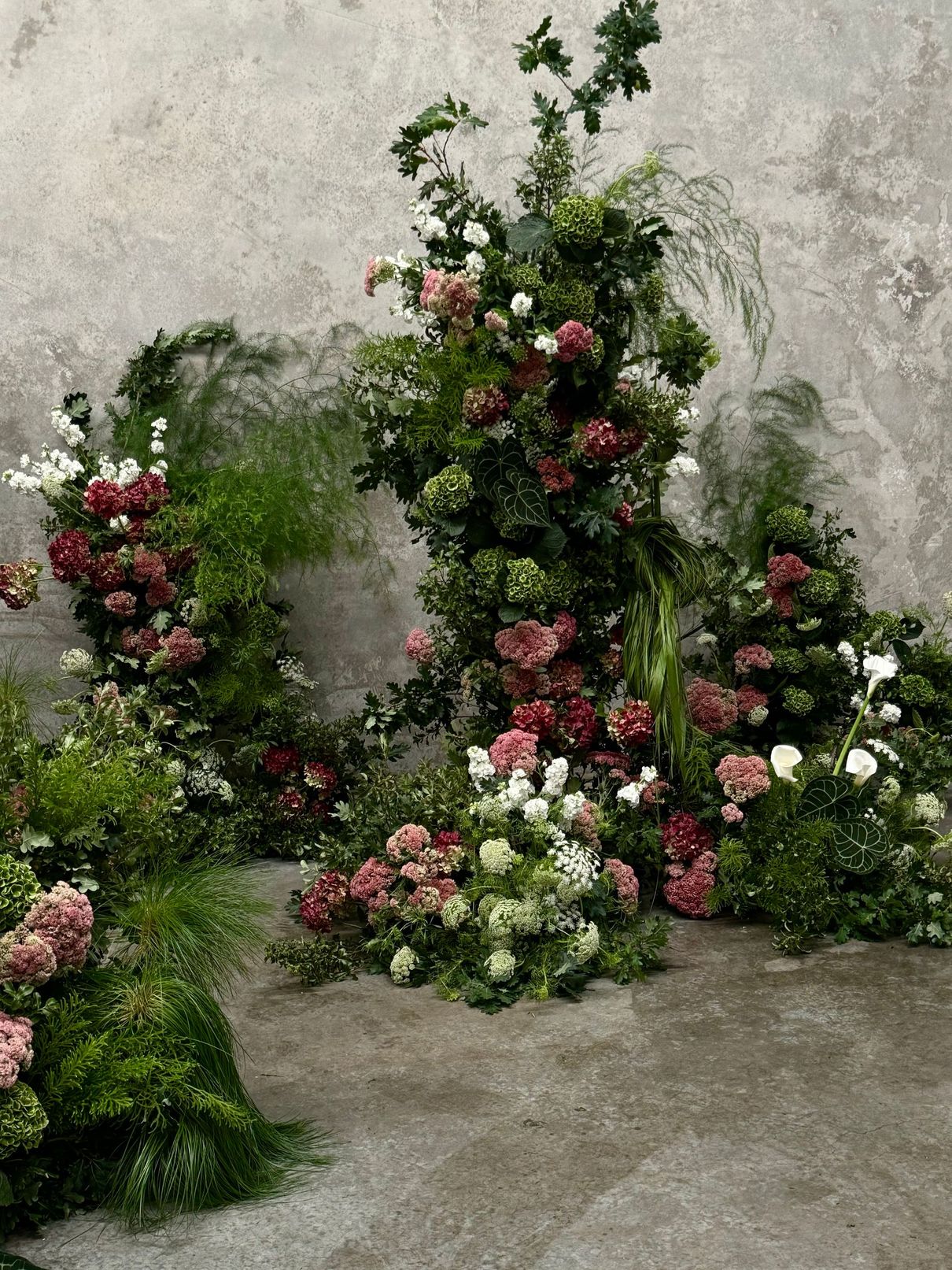 Flower arrangements with pink, white, and red blooms against a gray wall and floor