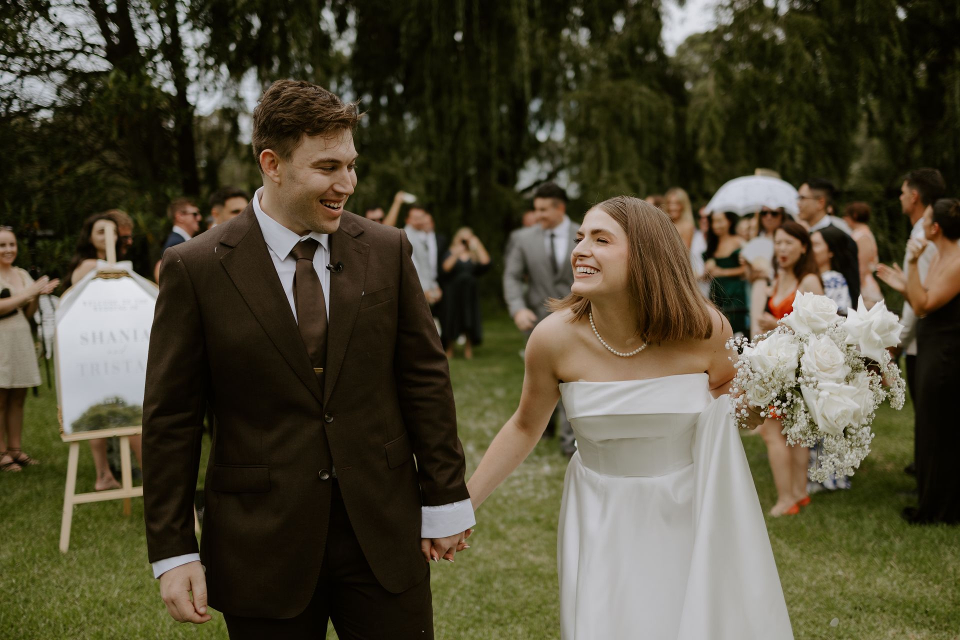Bride and groom walking hand in hand at an outdoor wedding ceremony, smiling at each other