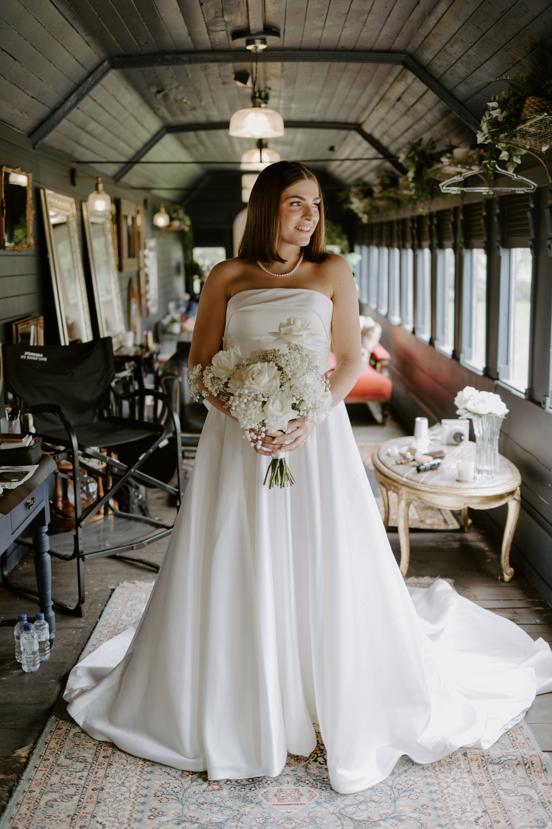 Bride in a white strapless gown holding a bouquet inside a vintage train car